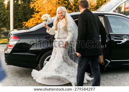 happy brunette groom and blonde bride near black solid rich car