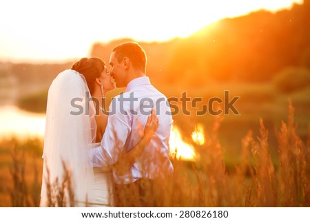 groom  and  bride is hugging and kissing on the background beautiful sunset on the lake