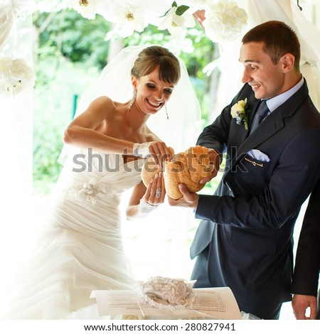 smiling groom and bride is  tearing bred on the  background white curtains