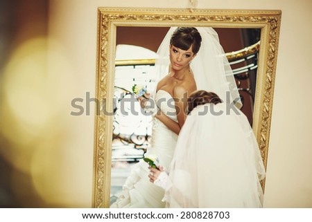 bride in white dress holding flower and looking at the miror