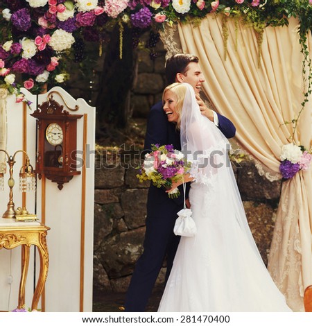 wonderful stylish rich happy bride and groom huging look et each other at a wedding ceremony in  garden near arch with flowers