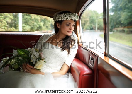 beautiful stylish luxury bride in crown holding bouquet of orchids and sitting in car