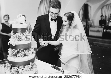 couple is cutting tasty cake decorated with adorning swans , pink lilies and ribbons