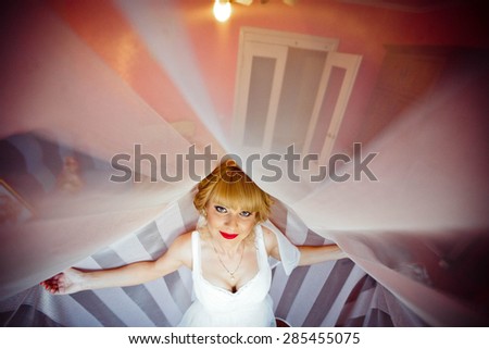 luxurious stylish smiling blonde bride with red lips is posing on the background of room