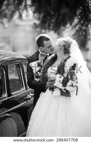 elegant groom kissing his beautiful blonde bride on the background of old city and a car