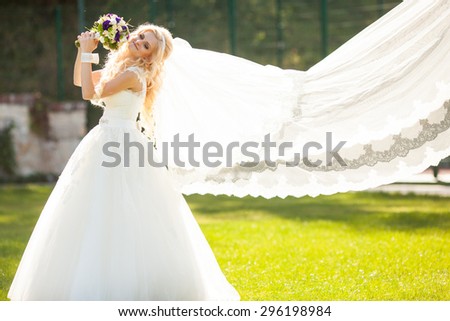 elegant stylish gorgeous blonde bride with veil on the background of trees in the park