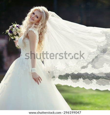 elegant stylish gorgeous blonde bride with veil on the background of trees in the park