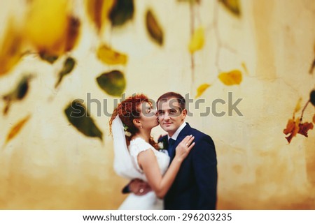grom huging kissing bride with red hair near wall outdoors Lviv