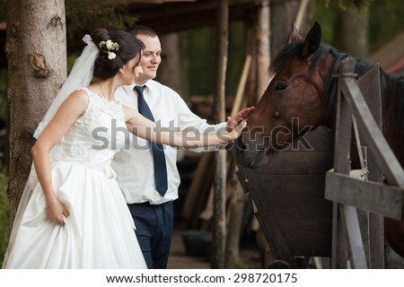 Cute happy bride and groom stroking a brown horse on a background of the forest