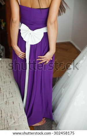 beautiful stylish bridesmaid in a violet dress helping bride in the morning in the room
