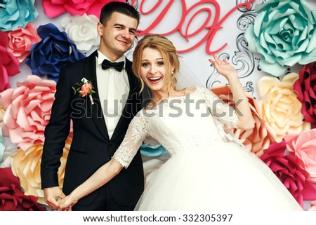 Happy emotional wedding couple holding hands and smiling groom and beautiful bride with flowers background