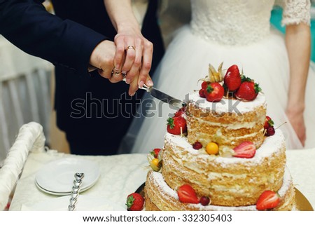 Happy wedding couple handsome groom and blonde bride carving delicious wedding cake