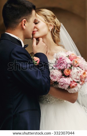 Happy handsome groom and blonde beautiful bride in white dress kissing under arc