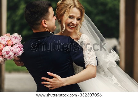 Happy handsome groom and blonde beautiful bride in white dress hugging under arc