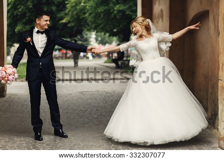 Happy handsome groom and blonde beautiful bride in white dress dancing under arc