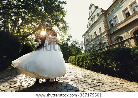 Beautiful young bride and handsome groom dancing outdoors near old mansion at sunset