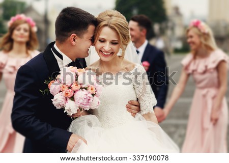 Handsome groom in suit hugging elegant blonde bride with bridesmaids and groomsmen