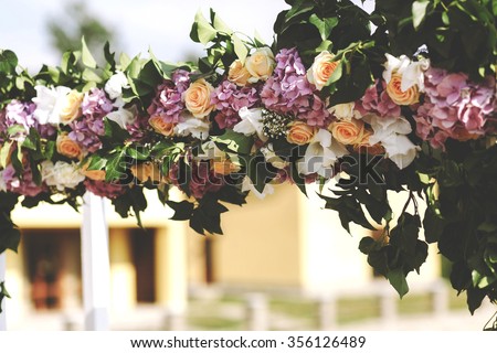 Luxury wedding arch with lush leaves, delicate roses and purple hydrangea outdoors. Wedding floristry