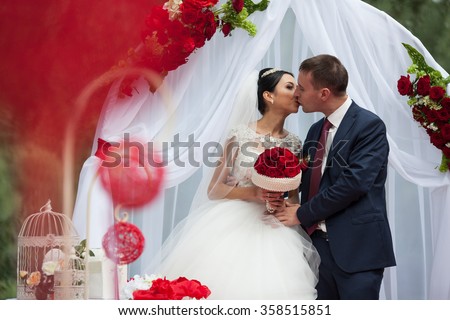 Happy newlywed romantic couple kissing at wedding aisle with red decorations and flowers
