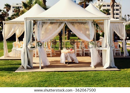 Luxurious wedding tent with haze peachy fabric and floral decorations near the palm trees and blue ocean