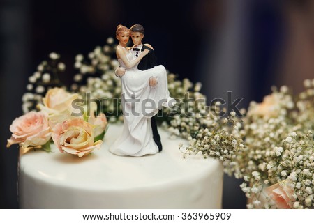 Funny figurines suite at a luxury wedding white cake decorated with fresh flowers.
