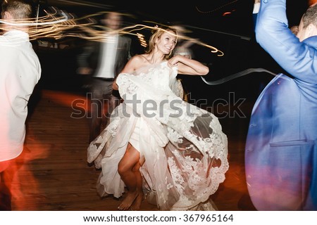 Young beautiful bride in white dress dancing with the guests in restaurant at her wedding evening