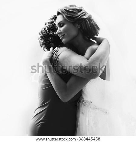 Beautiful blonde bride in her wedding day hugging her mother