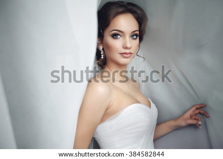Beautiful sexy bride in white dress posing under curtain