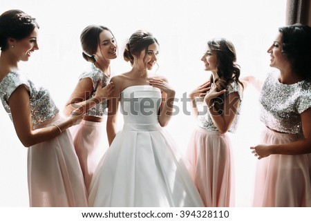 Beautiful bride & bridesmaids posing near window, wedding preparation