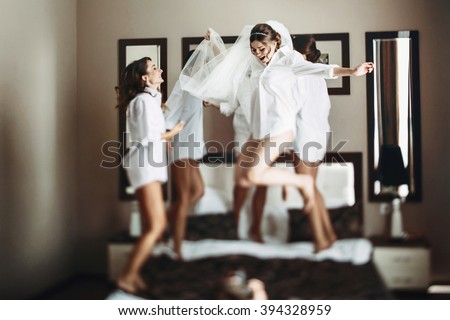 Sexy bride & bridesmaids jumping on bed before wedding