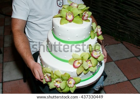Man holds a pretty wedding cake decorated with sugared greenery and flowers