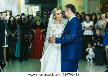 People surround a stylish wedding couple while they dance at the first time