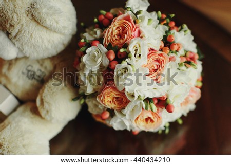 Pastel wedding bouquet of white and pink roses lies behind a plush toy bear