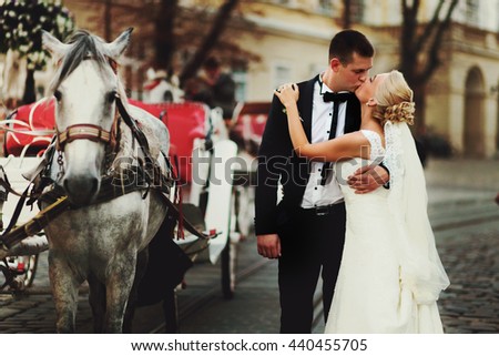 Groom kisses a bride behind a carriage