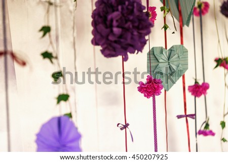 Green paper hearts and violet paper flowers hang on pink ribbons
