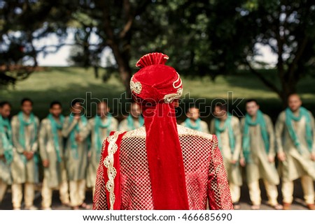 Hindu groom in red hat walks to groomsmen waiting for him outside
