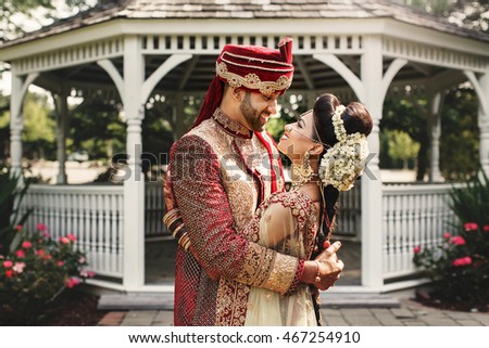 Handsome Indian groom in red hat holds in his hands a gorgeous bride