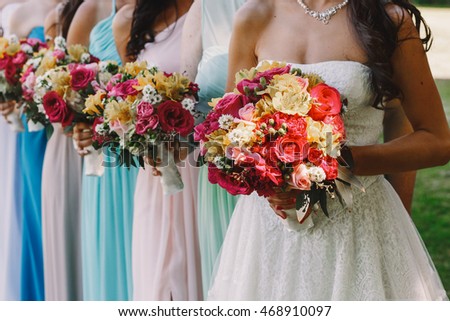 Bride with bronze skin holds her wedding bouquet before her chest while posing with bridesmaids