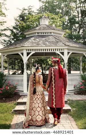 Look from behind at magnificent Indian wedding couple holding each other hands while walking around the garden