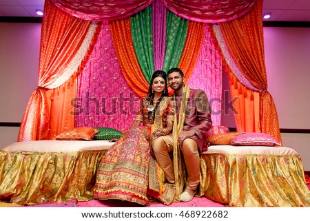 Pink, green and orange silk hangs over the Indian wedding couple sitting on the sofa