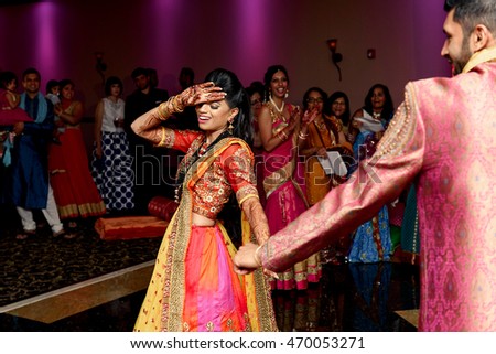 Stunning Indian bride hides her face behind her palm while dancing with a groom