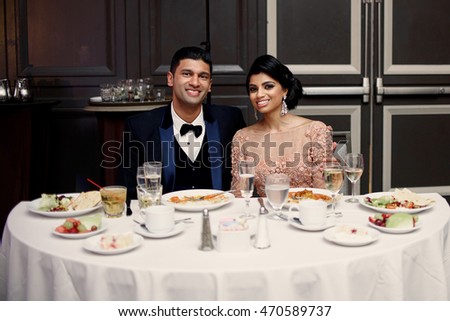 Happy Indian wedding couple sits at the white dinner table