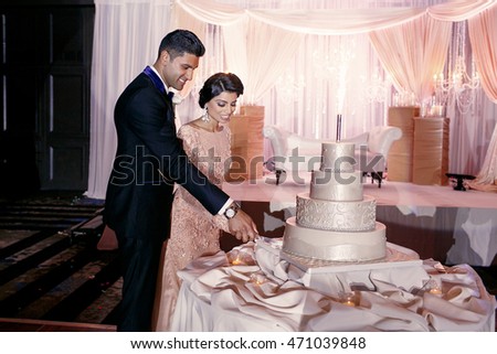 Fabulous Indian wedding couple cuts white cake standing on the silk cloth