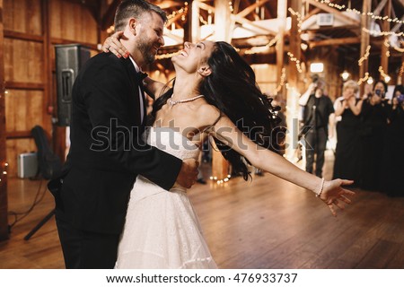 Bride shakes her dark hair while dancing with a groom in wooden hall