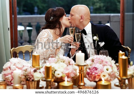 Beautiful newlyweds kiss holding glasses with champagne in their hands