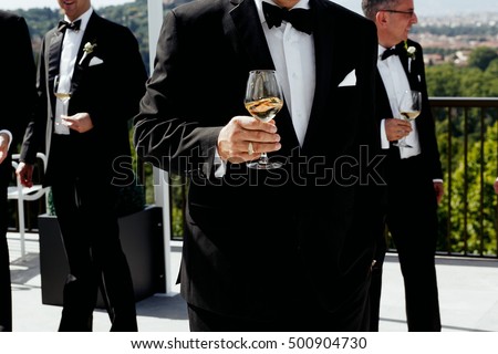 Closeup of glass with wine held by old man in black tuxedo