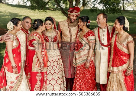 Happy parents surround magnificent Indian wedding couple dressed in golde and red tones