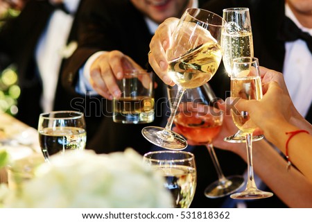 People clang glasses sitting at dinner table in sparkling lights