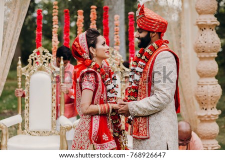Indian groom dressed in white Sherwani and red hat with stunning bride in red lehenga during the Saptapadi ceremony on Hindu wedding