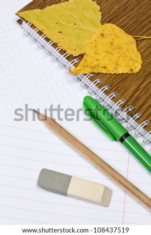 Opened school notebook and pencil, pen, eraser, leaves